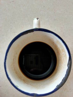 Beyaz kahve fincanının yukarıdan aşağı görüntüsü koyu bir demle, basit tasarımını ve içindeki koyu sıvıyı gösteriyor. Tanıdık bir sabah ritüelini yakalar, belki de zevk alır.