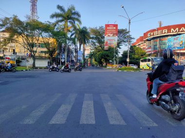Endonezya 'da, öğleden sonra ışıklarının altında bir kavşakta motosikletleri, yayaları ve trafiği gösteren canlı bir şehir manzarası günlük şehir hareketini vurguluyor. Malang, Doğu Java, Endonezya. 16 Haziran 2025