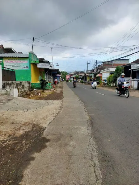 Küçük bir Endonezya kasabasının ana caddesinde sakin bir sabah başlıyor. Yerel halk motorsiklet ve geleneksel mağaza vitrinleriyle yumuşak, bulutlu bir gökyüzü altında günlük hayatı yakalıyor. Malang, Doğu Java, Endonezya. 19 Haziran 2025