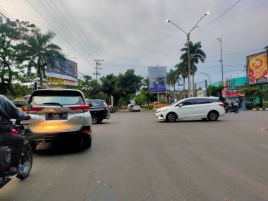 Malang, Doğu Java 'da hareketli bir kavşak, bulutlu bir gökyüzü altında günlük hayatın ritmini arabalar, motosikletler ve sokak sahneleriyle gösteriyor. 24 Haziran 2025