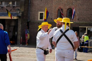 Alkmaar, Hollanda 16 Mart 2025: Waagplein Meydanı 'nda peynir tekerlekleri taşıyan Hollanda' nın beyaz üniformalı ve saman şapkalı peynir taşıyıcılarının yer aldığı geleneksel Alkmaar Peynir Pazarı 'nın (Kaasmarkt) editoryal görüntüleri. 