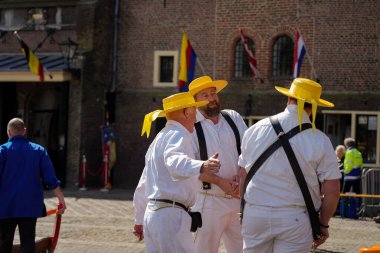Alkmaar, Hollanda 16 Mart 2025: Waagplein Meydanı 'nda peynir tekerlekleri taşıyan Hollanda' nın beyaz üniformalı ve saman şapkalı peynir taşıyıcılarının yer aldığı geleneksel Alkmaar Peynir Pazarı 'nın (Kaasmarkt) editoryal görüntüleri. 