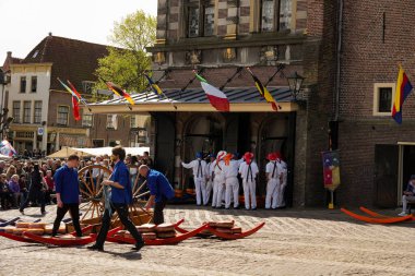 Alkmaar, Hollanda 16 Mart 2025: Waagplein Meydanı 'nda peynir tekerlekleri taşıyan Hollanda' nın beyaz üniformalı ve saman şapkalı peynir taşıyıcılarının yer aldığı geleneksel Alkmaar Peynir Pazarı 'nın (Kaasmarkt) editoryal görüntüleri. 
