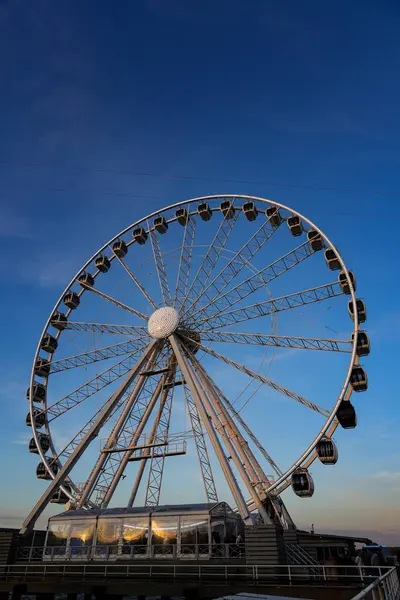 Hollanda, Lahey 'de günbatımında dönme dolabın manzarası. Altın saat ışığı sıcak ve atmosferik bir sahne yaratır. Renkli gökyüzüne karşı tekerleğin siluetini vurgular.. 