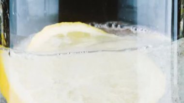 A lemon slice is dropped into sparkling water, creating an explosion of bubbles that rise vigorously