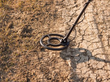 A metal detector hovers over parched soil, revealing potential buried artifacts clipart