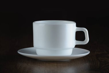 Boş bir beyaz fincan ve çay tabağı, koyu ahşap bir yüzeyde dinleniyor.