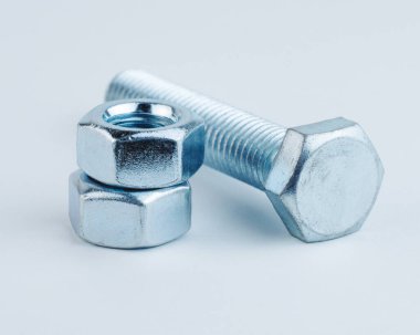 Bir çelik cıvata, düz beyaz bir yüzeyde altıgen bir fındığın yanında yatar.