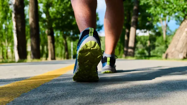 Bir insan açık gökyüzünün altında asfalt bir yol boyunca durmadan yürür.