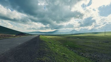 Yeşil tarlalar ve dağların arasından geçen manzaralı bir yol. Yüksek kalite fotoğraf