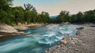 Rengarenk bir günbatımı gökyüzünün altındaki ağaçların arasından süzülen huzurlu bir nehir.