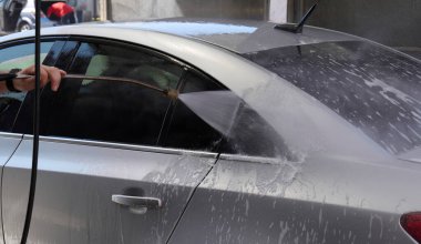 Dışarıdaki araba yıkama etkinliği sırasında gümüş bir sedanın üzerine su püskürtülür. Yüksek kalite fotoğraf