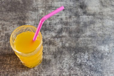 Tazeleyici portakal suyu, dokulu bir yüzeyde pembe bir pipetle servis edilir. Yüksek kalite fotoğraf