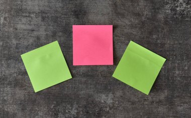 Pembe ve yeşil renkli üç yapışkan nota koyu bir arka planda oturur.