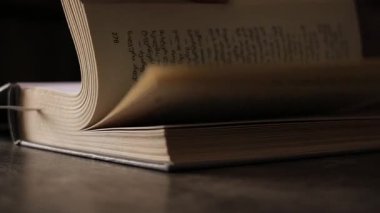 Sayfalar yavaş döner, ahşap bir yüzeydeki yumuşak ışıkla aydınlatılır.