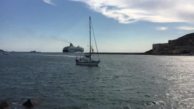 Arka planda büyük bir gemi gezisi olan küçük bir yelkenli.