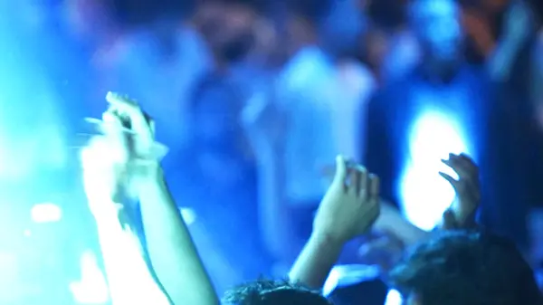  Konserde kalabalık el ele tutuşup dans ediyor. İnsanların elleri havada dans ediyor ve müziğin tadını çıkarıyor.