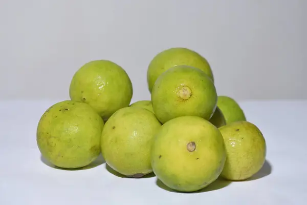 Canlı bir taze limon kümesi. Temiz beyaz bir yüzeye gelişigüzel istiflenmiş yeşil ve ince sarı renklerin karışımını sergiliyor. Bu parlak ve lezzetli görüntü mutfak temaları, sağlıklı beslenme, taze ürün, narenciye ve konseptler için mükemmeldir.