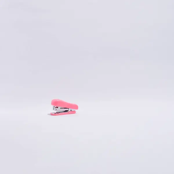 Canlı, parlak pembe bir mini zımba merkezi olarak temiz, kıvrımlı, izole beyaz bir arka plana yerleştirilir ve minimalist ve profesyonel bir stüdyo çekimi yaratır.