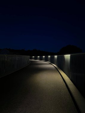 Uzağa uzanan yumuşak ışıklarla aydınlatılmış pürüzsüz asfalt yürüyüş yolu. Temiz ve modern bir şehir merkezi, şehir tasarımı, yönü veya arka plan kullanımı için harika.