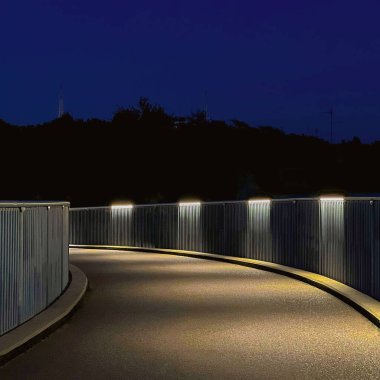 Çağdaş ışıklarla aydınlanan kavisli yaya yolu derin mavi bir gece gökyüzü altında. Arkaplan, kentsel tasarım ve yönelimsel veya kavramsal temalar için ideal.