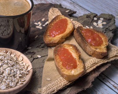 Siyah bir bardak kahve, domatesli tost ekmeği, yuvarlanmış yulaf ve ahşap dokular ile kırsal kahvaltı sahnesi, sıcacık, doğal bir sabah havasını çağrıştırıyor.