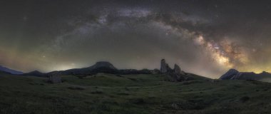 Palencia ve Cantabria arasındaki Piedrasluengas Geçidi 'ndeki kayalık tepeler ve yeşil çayırlar üzerinde samanyolu kemeri. Canlı galaktik çekirdeğiyle temiz bir gece göğü.