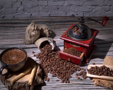 Öğütücü ve kahve çekirdekleri tahtanın üzerinde ve kırsal tuğla arka planda, kahvaltıda kahve ve kurabiye ile, seçici ışıklandırmayla