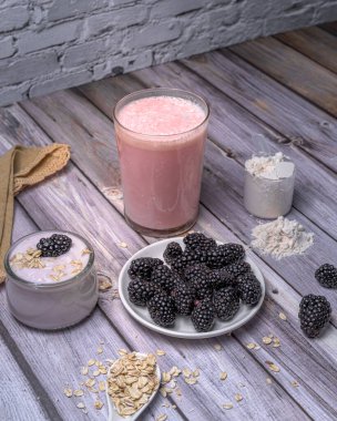 Sağlıklı kahvaltı malzemeleri böğürtlen, yoğurt, yulaf ve kırsal ahşap masa üzerinde protein tozu. Doğal ve besleyici smoothie hazırlama konsepti