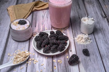 Sağlıklı kahvaltı malzemeleri böğürtlen, yoğurt, yulaf ve kırsal ahşap masa üzerinde protein tozu. Doğal ve besleyici smoothie hazırlama konsepti