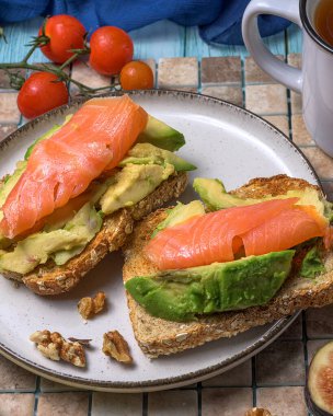 Bitki çayıyla sağlıklı kahvaltı, füme somon, ceviz ve kırsal bir masada servis edilen taze incirle kaplı avokado tostu.