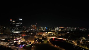 Adelaide City, Güney Avustralya, çarpıcı 4K hava aracı görüntülerinde gece çekiliyor. Bu canlı manzara aydınlık şehir silueti, modern mimari, River Torrens yaya köprüsü ve Festival Plaza 'nın renkleriyle parıltısını sergiliyor. Trafikten