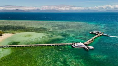 Green Island 'ın hava görüntüleri. Queensland, Avustralya açıklarındaki Büyük Set Resifi' ndeki bir mercan mağarası. Sahne turkuaz suları, uçan resifler, beyaz kumsallar, uzun bir iskele ve iskeleyi ve yoğun tropikal yağmur ormanlarını yakalıyor. Popüler.