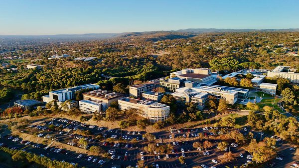 The image features the university Central Park, lecture buildings, carparks, and forested surroundings, all glowing in warm light. A scenic view of the education infrastructure embedded in natural bushland.