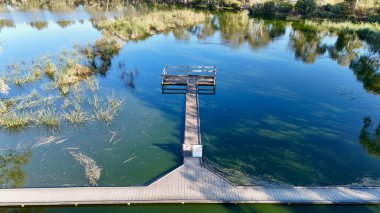 Güney Avustralya, Barker Dağı 'ndaki Laratinga Wetlands durgun göletleri, çeşitli kuş yaşamları ve yürüyen patikalarıyla bilinen sakin bir doğa koruma alanıdır. Bu hava aracı görüntüsü, durgun su ve su bitkilerinin üzerindeki tahta tahta kaldırımların yükseltilmiş görüntüsünü yakalıyor.