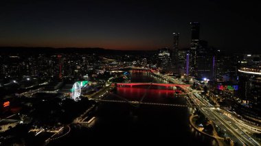 Brisbane CBD 'nin Queensland, Avustralya' daki hava fotoğrafında Brisbane Nehri 'nden yansıyan şehir ışıkları, Brisbane Çarkı, ışıldayan köprüler, gökdelenler ve canlı South Bank bölgesi yer alıyor. Brisbane 'in büyüleyici manzarası