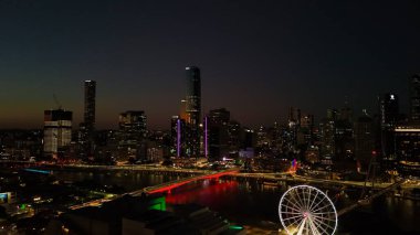 Brisbane CBD 'nin Queensland, Avustralya' daki hava fotoğrafında Brisbane Nehri 'nden yansıyan şehir ışıkları, Brisbane Çarkı, ışıldayan köprüler, gökdelenler ve canlı South Bank bölgesi yer alıyor. Brisbane 'in büyüleyici manzarası