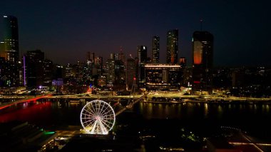 Brisbane CBD 'nin Queensland, Avustralya' daki hava fotoğrafında Brisbane Nehri 'nden yansıyan şehir ışıkları, Brisbane Çarkı, ışıldayan köprüler, gökdelenler ve canlı South Bank bölgesi yer alıyor. Brisbane 'in büyüleyici manzarası