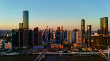 Günbatımında Queensland, Avustralya 'da Brisbane CBD' nin hava görüntüsünde parlayan şehir silueti, yüksek binalar, Brisbane 'nin ikonik tekerleği ve Brisbane Nehri yer alıyor. Altın saat boyunca yakalanan bu resim canlı kenti vurguluyor.
