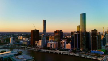 Günbatımında Queensland, Avustralya 'da Brisbane CBD' nin hava görüntüsünde parlayan şehir silueti, yüksek binalar, Brisbane 'nin ikonik tekerleği ve Brisbane Nehri yer alıyor. Altın saat boyunca yakalanan bu resim canlı kenti vurguluyor.