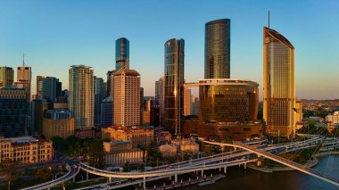Günbatımında Queensland, Avustralya 'da Brisbane CBD' nin hava görüntüsünde parlayan şehir silueti, yüksek binalar, Brisbane 'nin ikonik tekerleği ve Brisbane Nehri yer alıyor. Altın saat boyunca yakalanan bu resim canlı kenti vurguluyor.