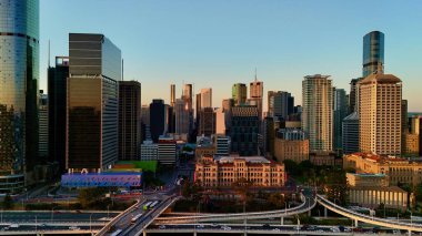 Günbatımında Queensland, Avustralya 'da Brisbane CBD' nin hava görüntüsünde parlayan şehir silueti, yüksek binalar, Brisbane 'nin ikonik tekerleği ve Brisbane Nehri yer alıyor. Altın saat boyunca yakalanan bu resim canlı kenti vurguluyor.