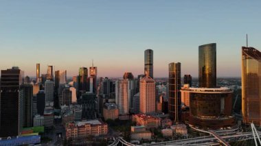 Günbatımında Queensland, Avustralya 'da Brisbane CBD' nin hava görüntülerinde parlayan şehir silueti, yüksek binalar, ikonik Brisbane Çarkı ve Brisbane Nehri yer alıyor. Altın saat boyunca yakalanan bu resim canlı kenti vurguluyor.