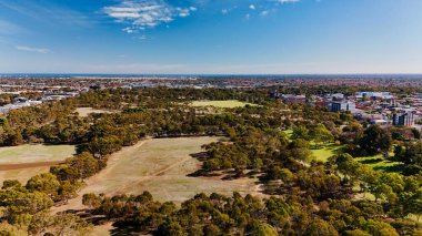 Güney Avustralya Adelaide City 'de bulunan Veale Park, Park 21' in yüksek çözünürlüklü hava aracı görüntülerinde geniş spor alanları, ağaç kaplı parklar ve Güney Terrace boyunca uzanan modern şehir silueti yer alıyor. Arkaplan sergileniyor Yuvarlanan Lofty Dağı