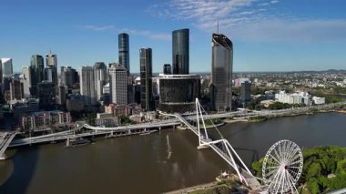 Queensland, Avustralya 'daki Brisbane City' nin gündüz hava görüntüsü. Görüntü, kentin modern silueti, Brisbane Nehri, önemli köprüler ve parlak mavi gökyüzü altında yükselen ticari binaları gözler önüne seriyor. Merkezi ticaretin net ve geniş bir görüntüsü
