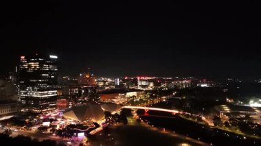 Adelaide City, Güney Avustralya, çarpıcı 4K hava aracı görüntülerinde gece çekiliyor. Bu canlı manzara aydınlık şehir silueti, modern mimari, River Torrens yaya köprüsü ve Festival Plaza 'nın renkleriyle parıltısını sergiliyor. Trafikten