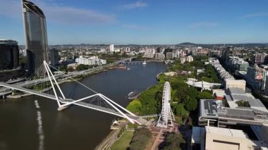 Queensland, Avustralya 'daki Brisbane City' nin gündüz hava görüntüsü. Görüntü, kentin modern silueti, Brisbane Nehri, önemli köprüler ve parlak mavi gökyüzü altında yükselen ticari binaları gözler önüne seriyor. Merkezi ticaretin net ve geniş bir görüntüsü