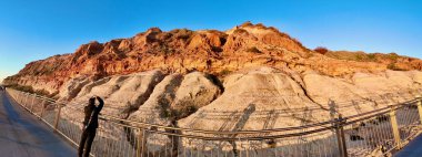 Port Noarlunga 'nın 180 derecelik panoramik görüntüsü Güney Avustralya' daki baş döndürücü sahil kayalıkları. Bu süpürücü görüntü, yıpranmış kırmızı kumtaşı oluşumları, yumuşak aşınmış kaya katmanları ve manzaralı yükseltilmiş tahta kaldırım üzerinde altın saat güneş ışığını yakalar.