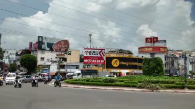 Ho Chi Minh City, Vietnam 'ın dinamik bir 4K sokak görüntüsü, kalabalık motosiklet ve araba trafiği, yol kenarı dükkanları ve caddeleri kaplayan uzun ağaçlarla günlük şehir yaşamını yakalıyor. Bu görüntülerde canlı enerji, kültürel çeşitlilik ve hızlı