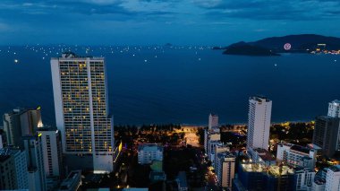 Vietnam, Khanh Hoa 'daki Nha Trang Sahili' nin çarpıcı hava manzarası, lüks sahil otelleri, altın kum, sakin mavi sular ve yemyeşil dağ sıraları ile canlı bir kıyı şehri manzarası sergiliyor. Akşam ışıkları kıyı şeridini aydınlatırken, şehir